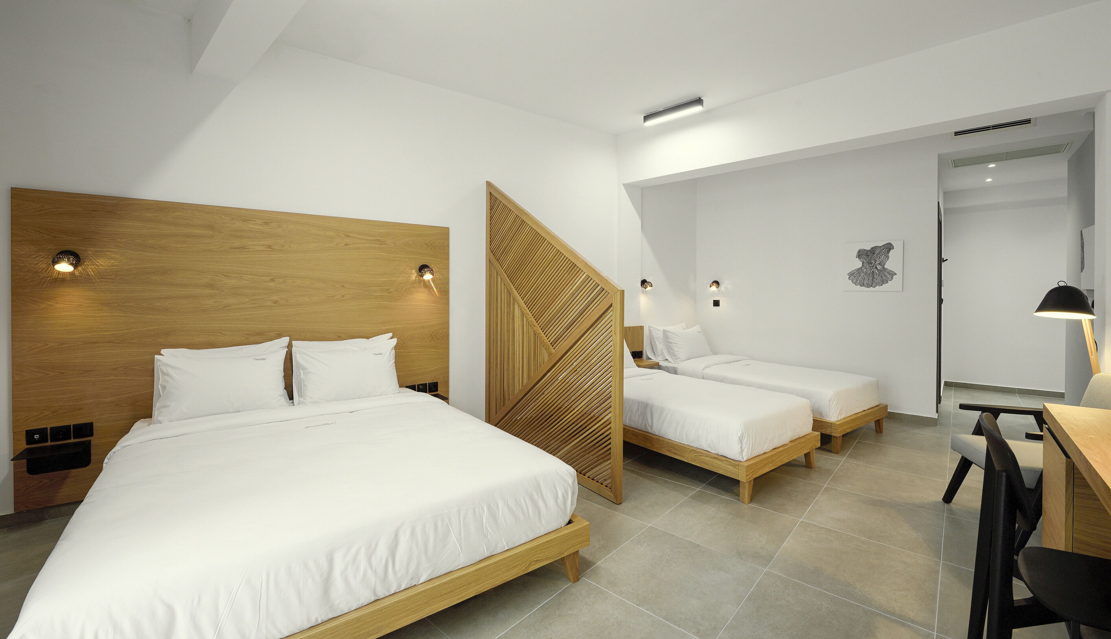 A hotel room with a large bed, two smaller beds, a desk, and a chair.