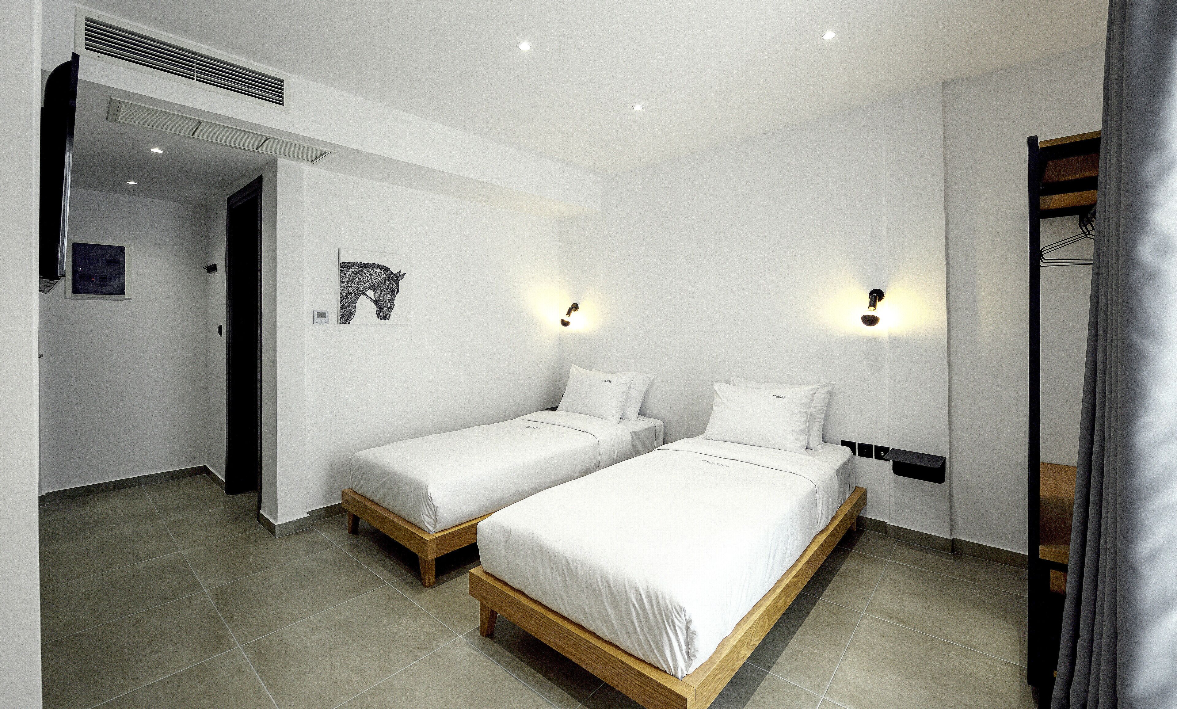 Una habitación de hotel con dos camas individuales, una obra de arte colgada en la pared y un respiradero en el techo.