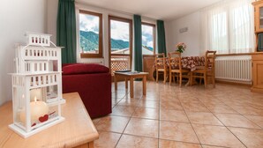 A cozy room with a dining area, a red sofa, a white lantern, and a view of mountains through the windows. - Apartment in the heart of Valle di Sole (Mezzana-Marilleva)