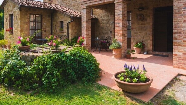A stone building with a tiled roof, a covered patio area, and potted plants. - Podere San Gregorio (Pienza)