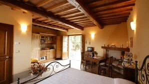 A bedroom with a bed, a desk, and a television. There is a wooden ceiling and a door leading to a kitchen. - Podere San Gregorio (Pienza)