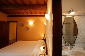Un dormitorio con cama, lámparas de noche, techo de madera y un baño con lavabo y espejo.