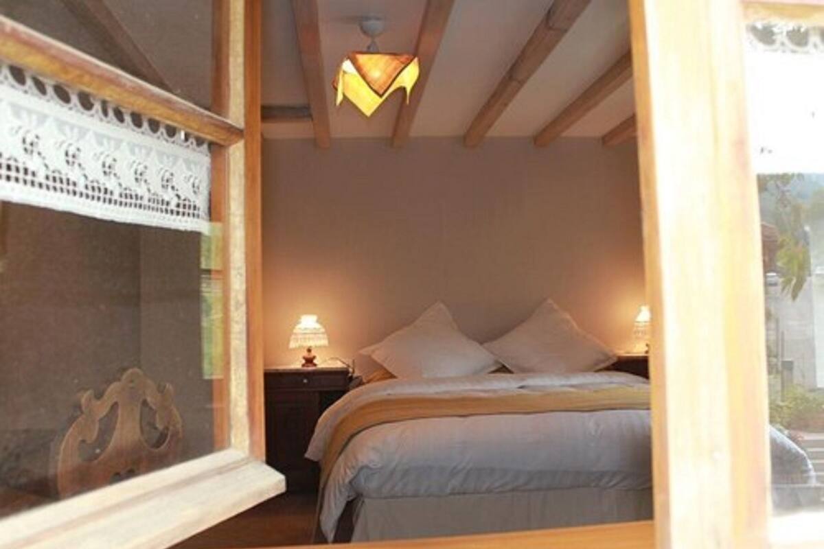 Un dormitorio con cama, dos lámparas de noche, un ventanal con marco decorativo y techo de madera.