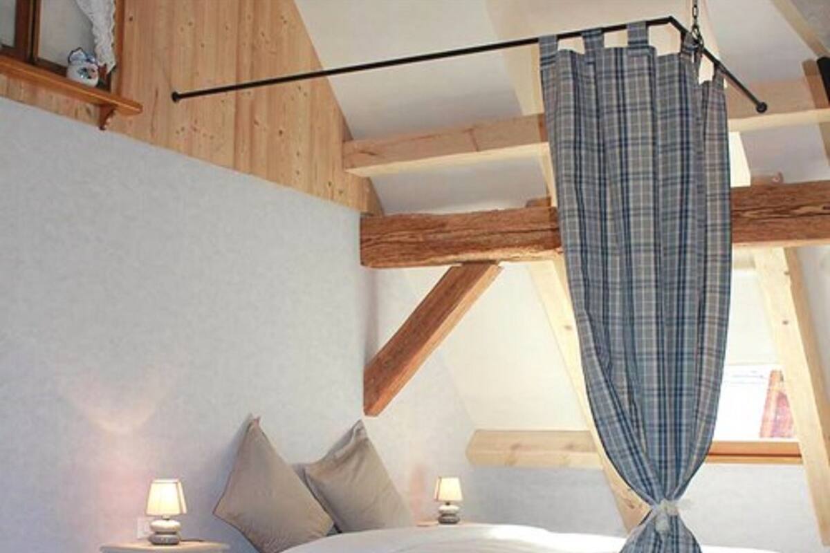 Un dormitorio con cama, dos mesitas de noche, una lámpara y una ventana con cortinas.