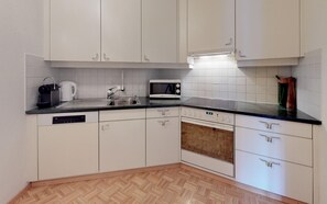 A kitchen with white cabinets, a microwave, a kettle, and a dishwasher.