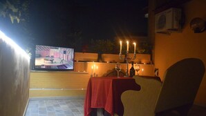 An outdoor seating area with a table set for two, candles, and a television screen displaying a show. - Boutique Roma D'Autore (Rome)