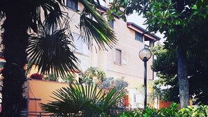 A courtyard with lush greenery, a building with a brick facade, and a street lamp. - Boutique Roma D'Autore (Rome)