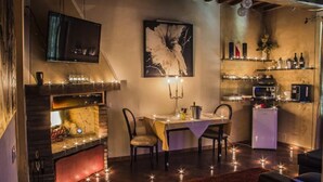 A cozy dining area with a table set for two, a television mounted on the wall, and a fireplace with a red mantle. - Boutique Roma D'Autore (Rome)
