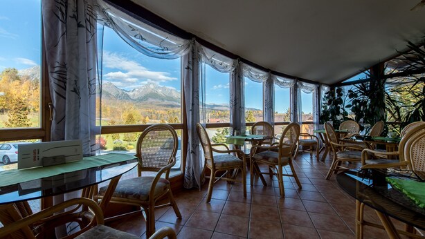 Un restaurante acogedor con mobiliario de mimbre y ventanas amplias que ofrecen vistas a la montaña.