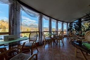 A cozy restaurant with wicker furniture and large windows offering mountain views. - Hotel Eufória (Nova Lesna)