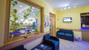 Un área de recepción con un ventanal grande, un mostrador de recepción, una zona de estar con dos sillas y un televisor montado en la pared.