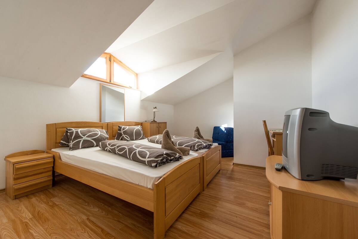 Quarto com cama de madeira, televisão e pequena mesa de trabalho.