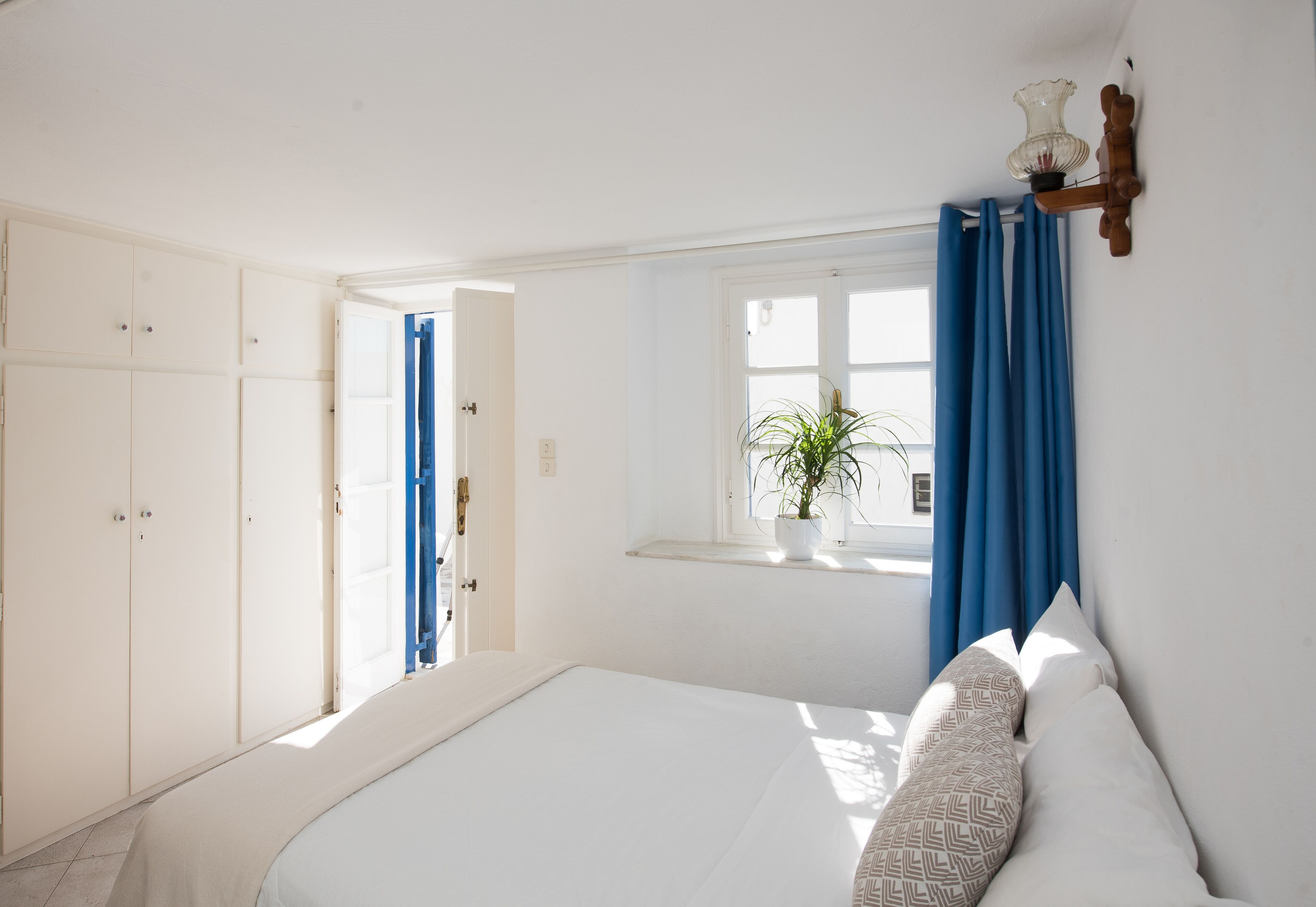 Un dormitorio con cama, ventana con cortinas, una planta en maceta y un armario.