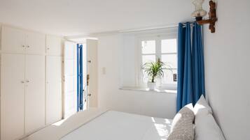 Un dormitorio con cama, ventana con cortinas, una planta en maceta y un armario.