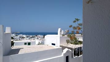 Vista de un pueblo costero con edificios blancos, cielo azul despejado y el mar al fondo.