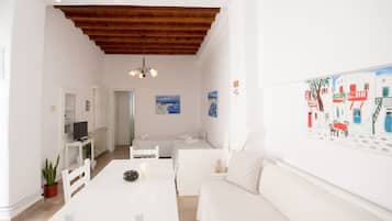 Un interior luminoso y blanco con techo de madera, una mesa de comedor, un sofá y un televisor sobre un soporte blanco.