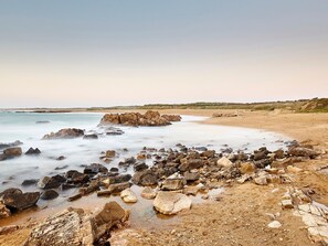 A coastal landscape with a rocky shoreline, calm sea, and a clear sky.