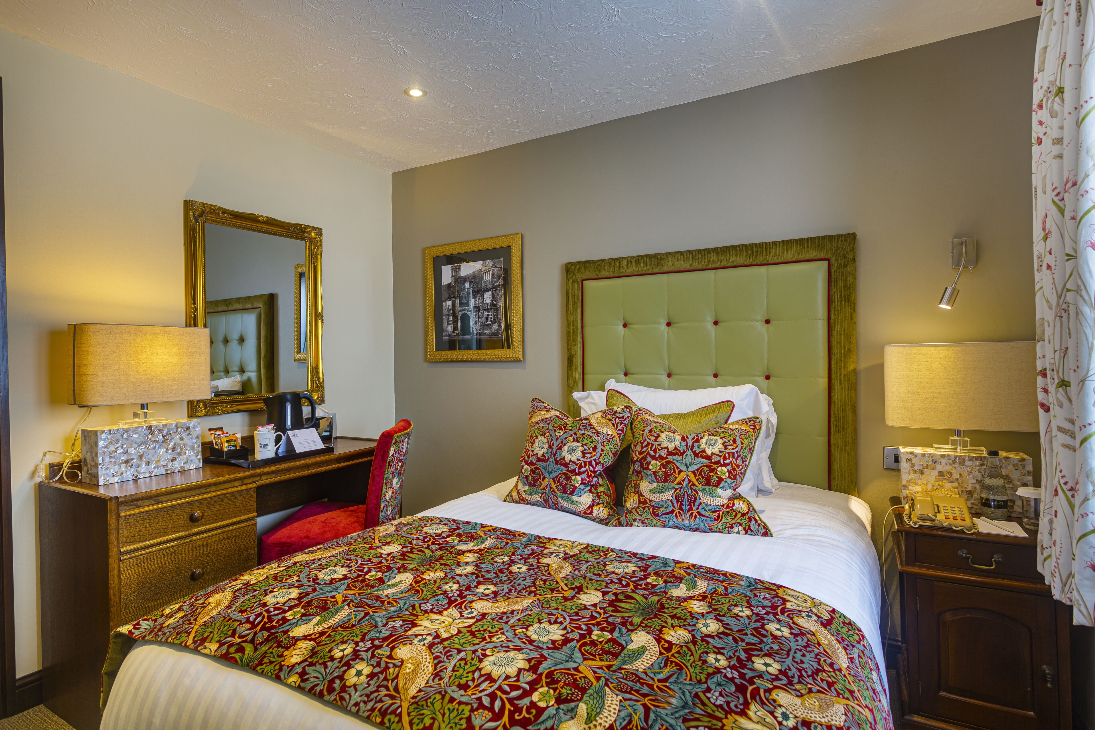 Hotelkamer met een groot bed, een dressoir, een bureau, een stoel, een spiegel en een nachtkastje met een lamp.