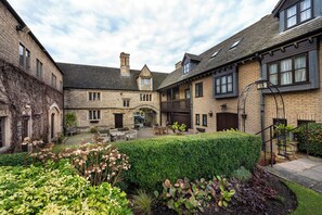 A courtyard with stone buildings, a bench, and a well-maintained hedge. - The Bell Inn Hotel, Stilton, Cambridgeshire (Peterborough)