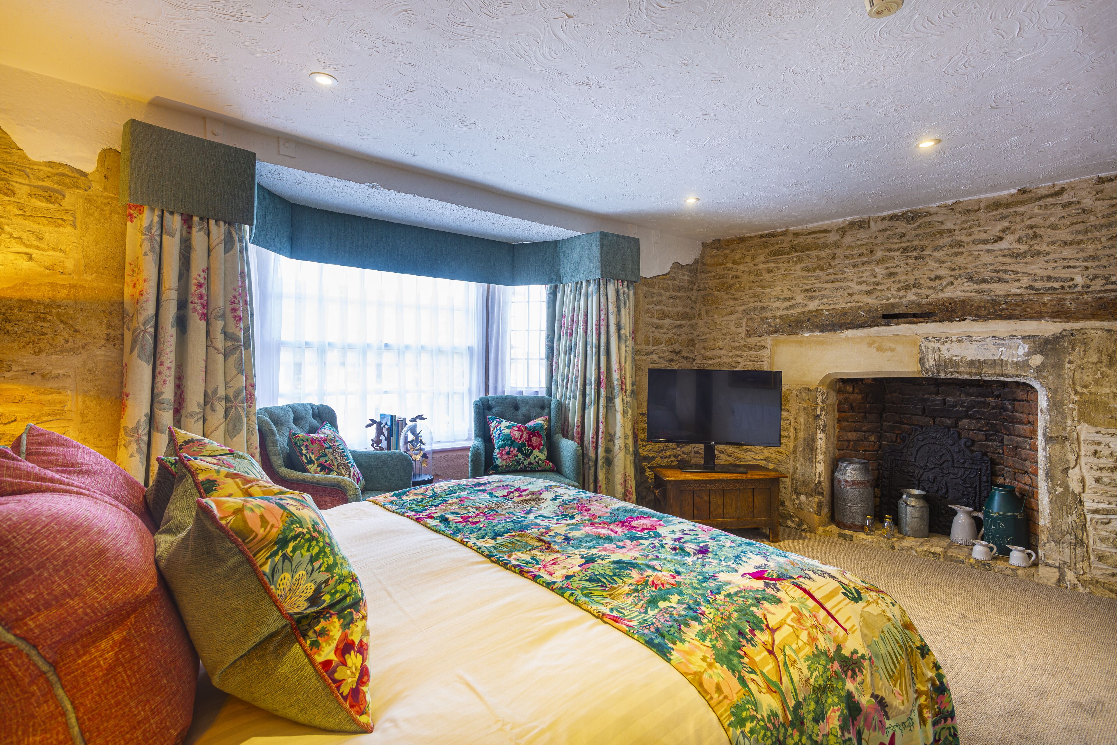 A room with a large bed, a chair, a television, and a fireplace.
