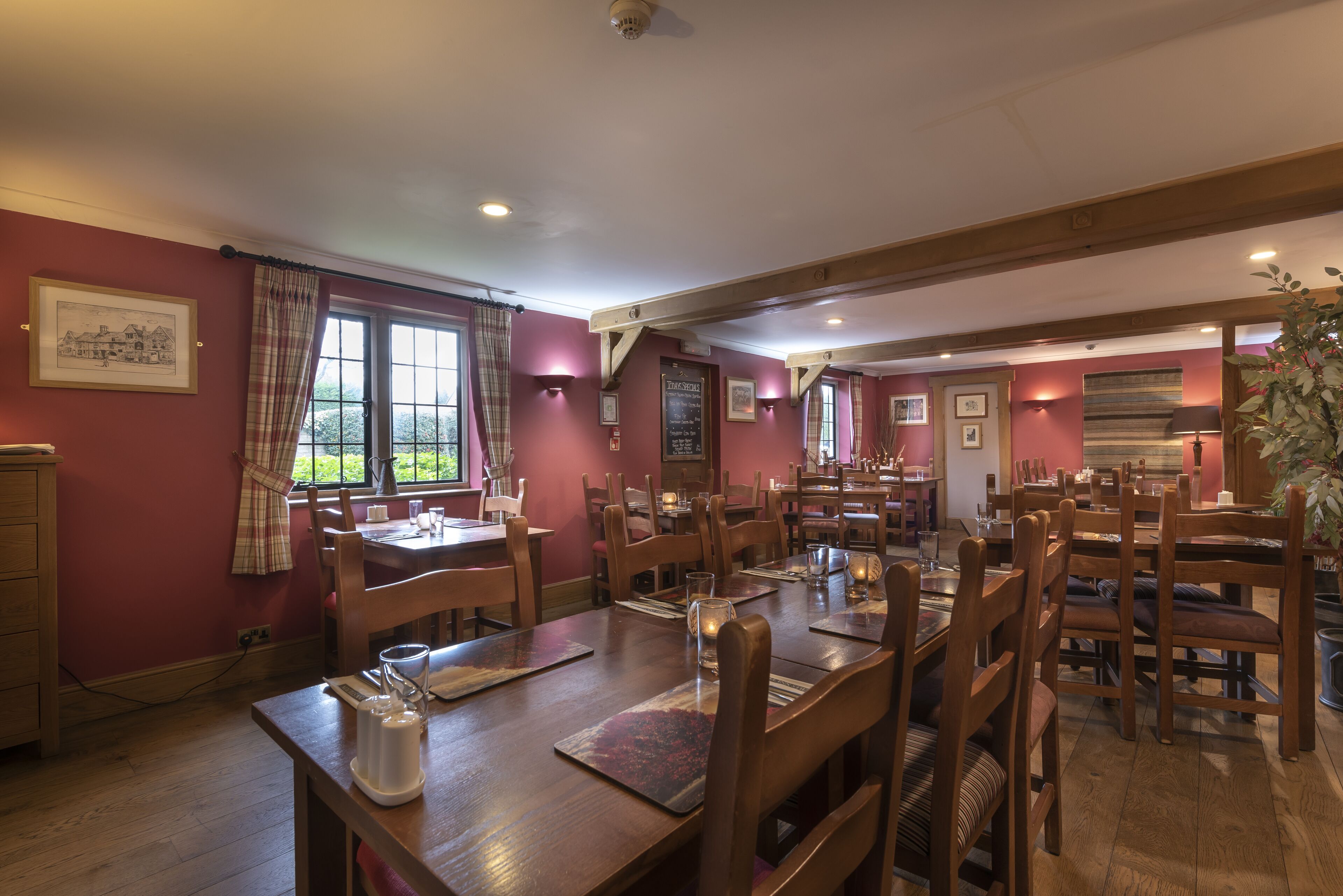 A dining area with wooden tables and chairs, a chalkboard menu, and a view of the outdoors through large windows.
