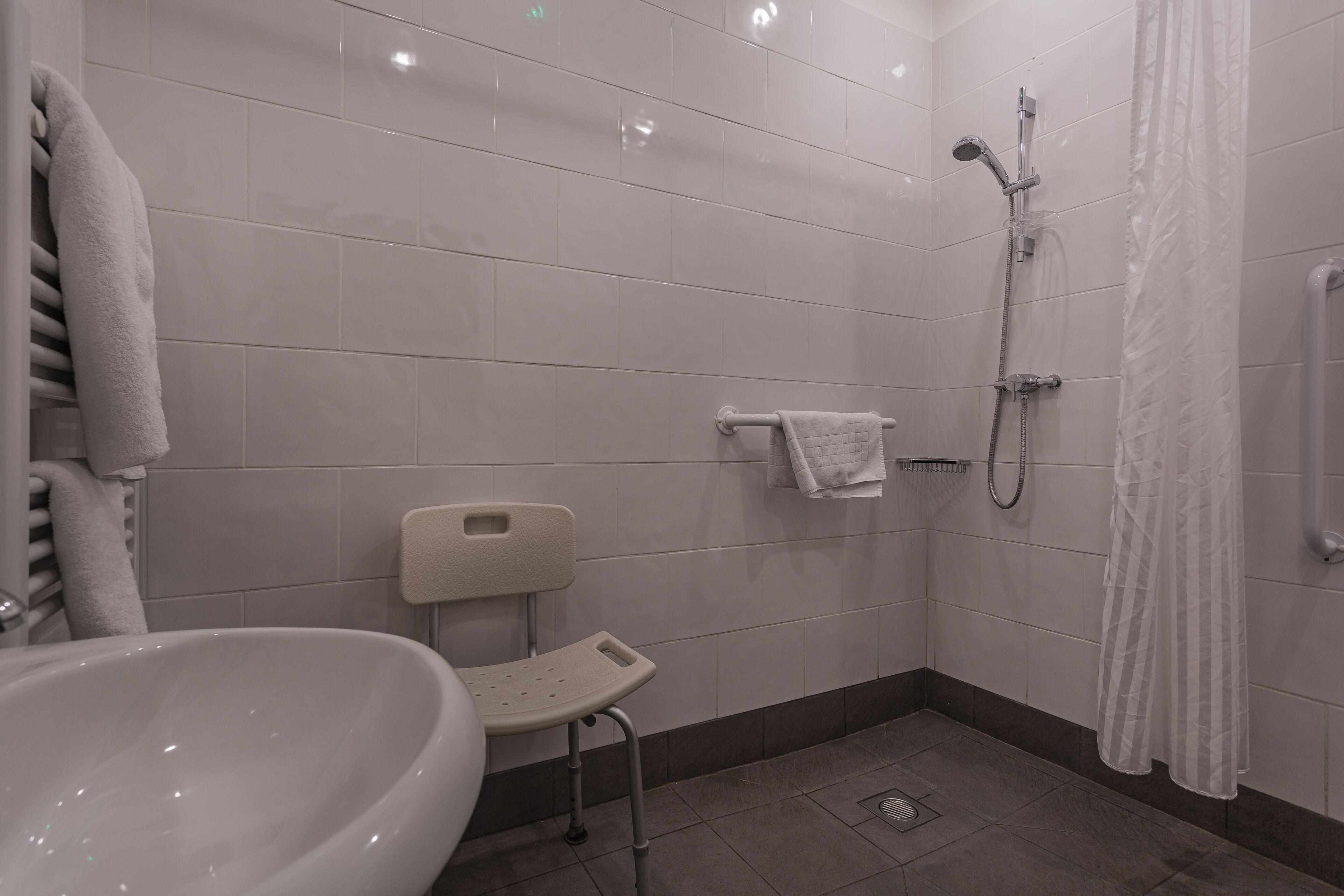 A bathroom with a white sink, a shower with a handheld showerhead, and a white towel rack.
