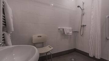 A bathroom with a white sink, a shower with a handheld showerhead, and a white towel rack.