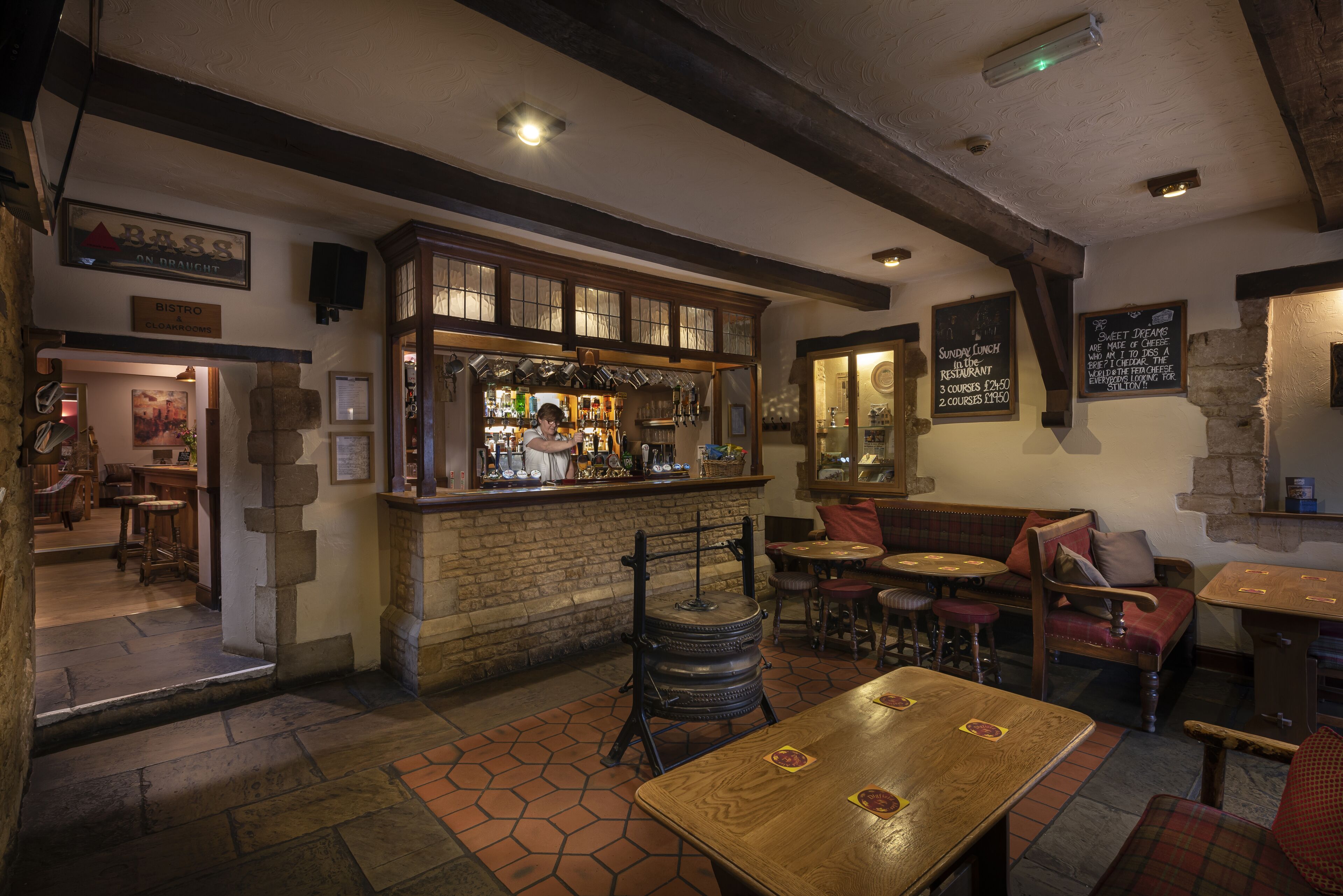 A rustic pub interior with wooden beams, a bar area, and seating arrangements.