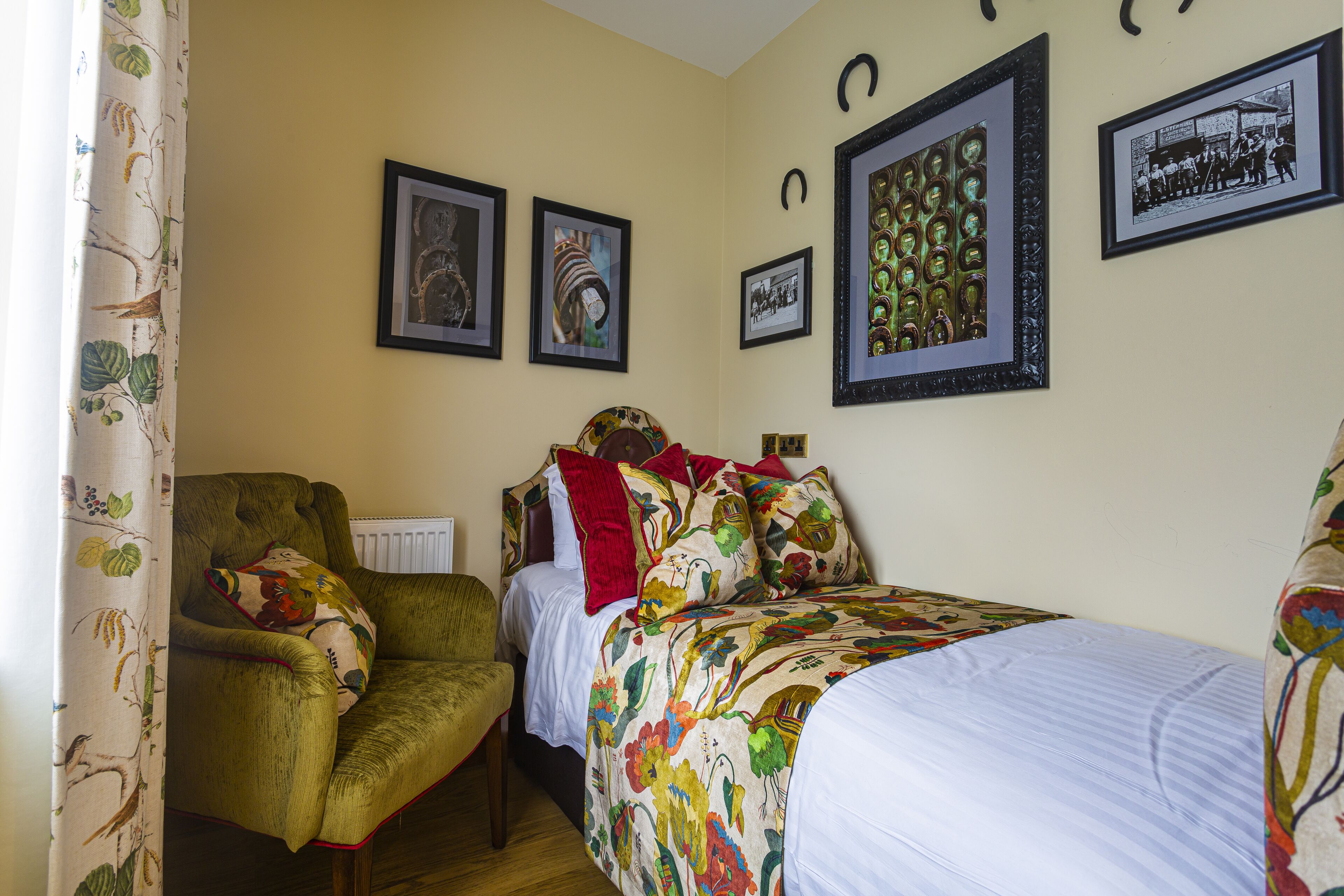 A bedroom with a bed, a chair, and a radiator. There are framed pictures on the wall.