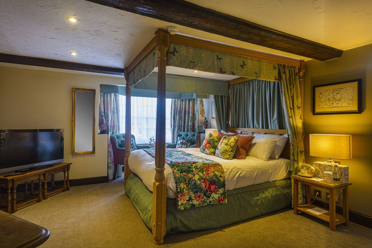 Una cama con dosel con ropa de cama floral, un televisor sobre un soporte de madera y un mapa enmarcado en la pared.