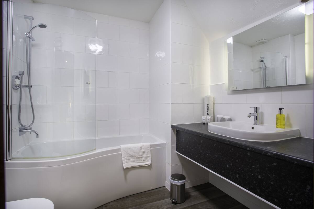 Un baño moderno con ducha envuelta en vidrio, una bañera blanca, un lavamanos con encimera negra y un espejo sobre el lavamanos.