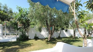 Un patio con muebles blancos, cerca blanca y árboles.