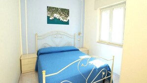 Un dormitorio con cama, mesita de noche, ventana y un cuadro colgado en la pared.