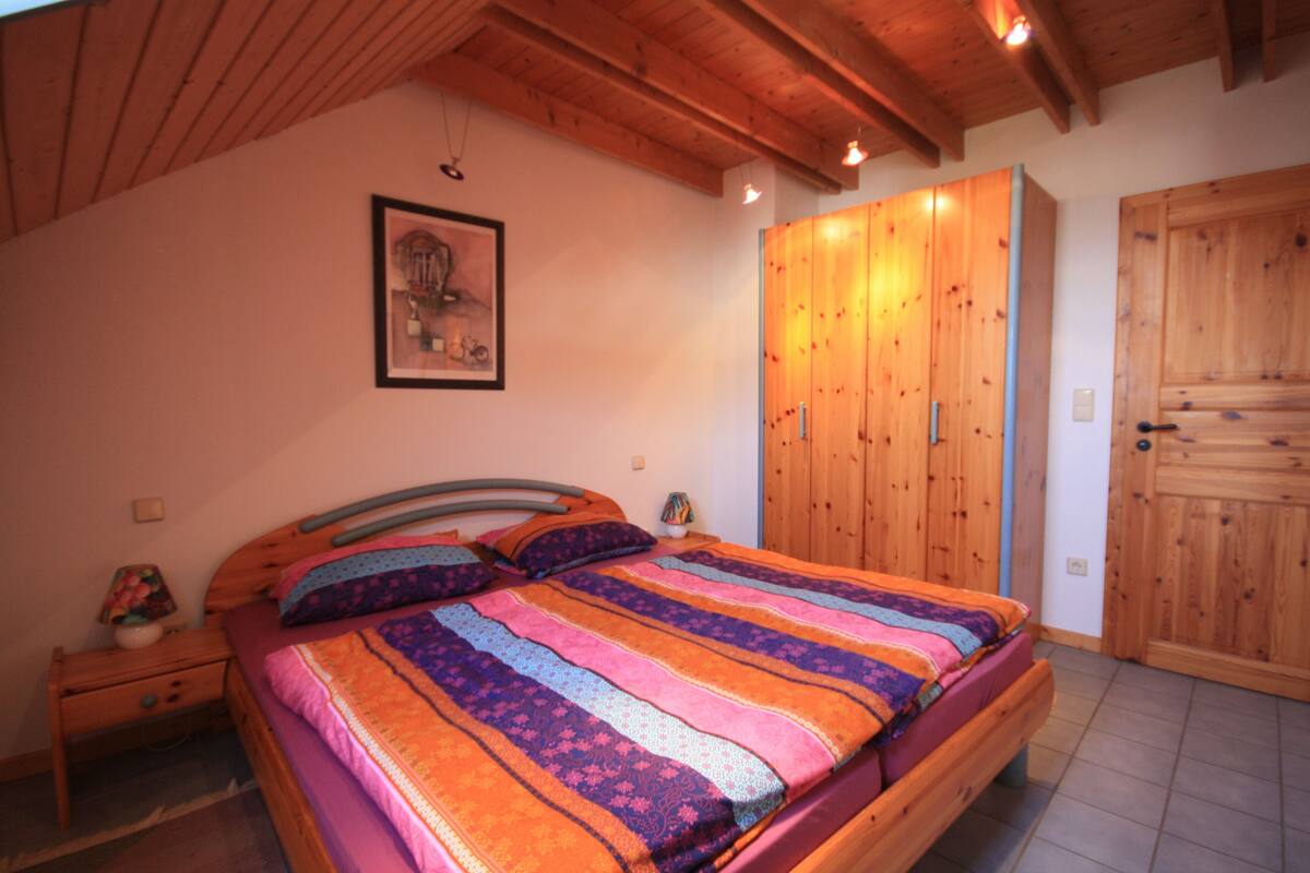 Een slaapkamer met een houten bed, nachtkastje, kledingkast en een ingelijste foto aan de muur.
