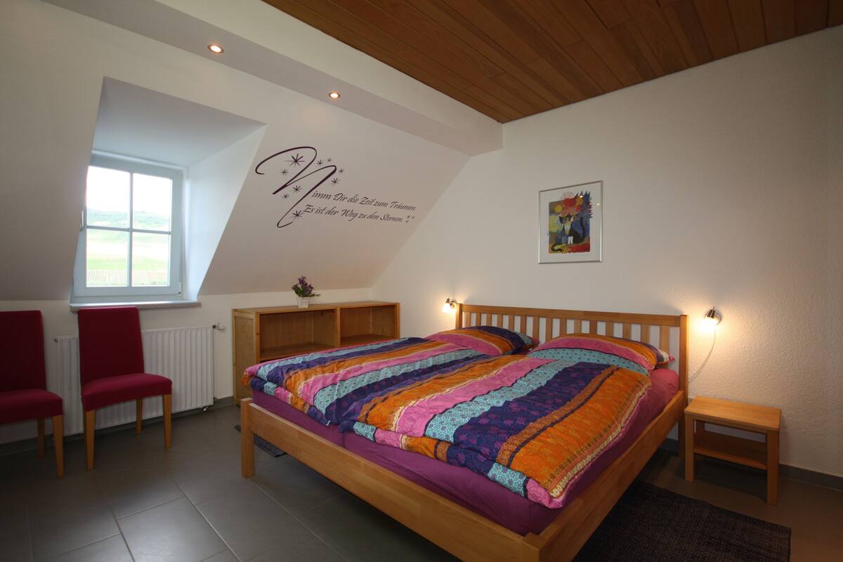 Een slaapkamer met een houten bed, een raam, een rode stoel en een klein nachtkastje.