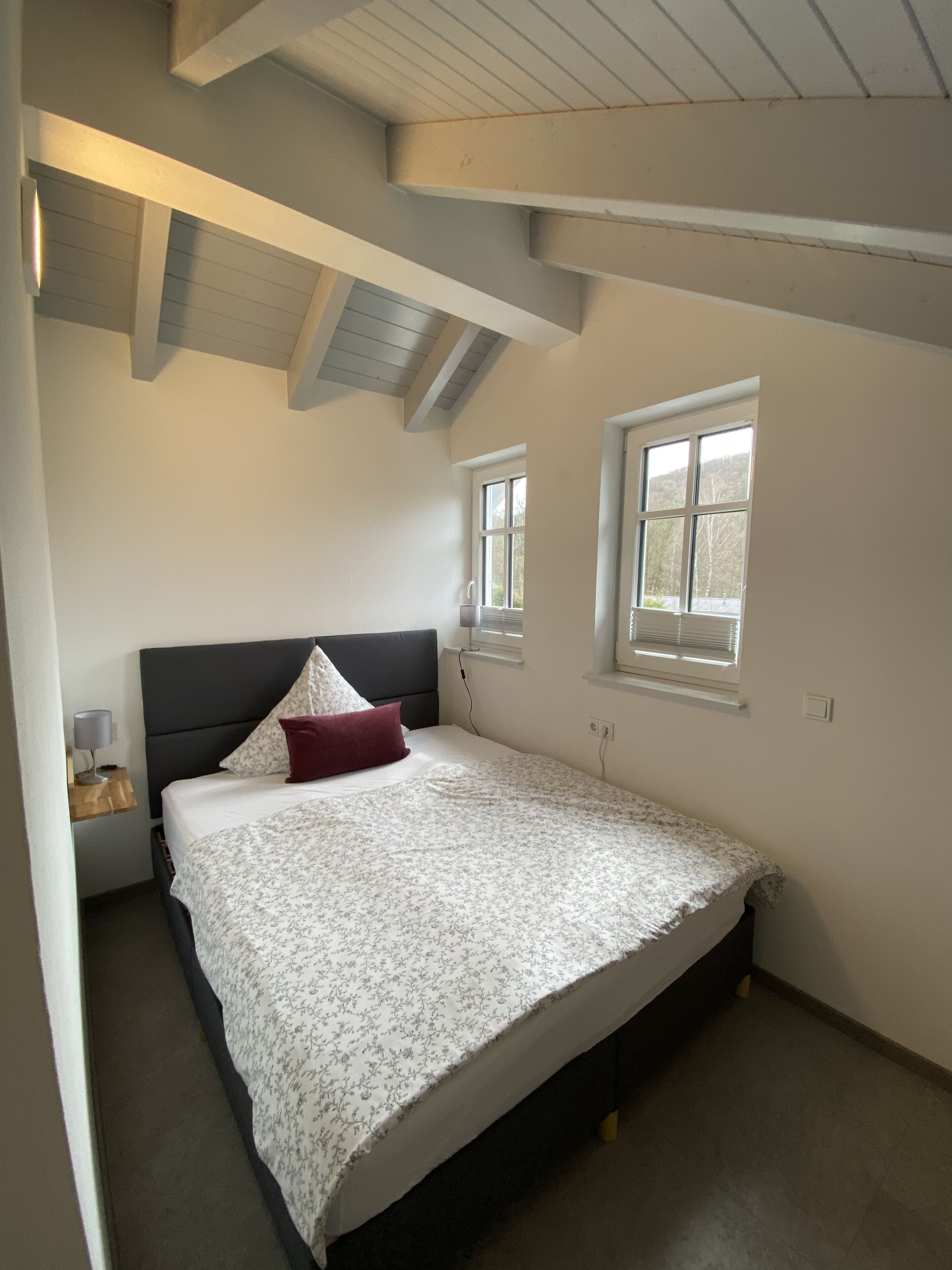 Un dormitorio con cama, mesita de noche, ventana y techo inclinado.
