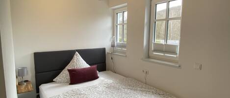 Un dormitorio con cama, mesita de noche, ventana y techo inclinado.