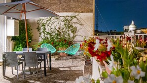 Un patio al aire libre con una mesa, sillas, un paraguas grande y plantas en macetas.