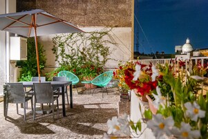 Un patio al aire libre con una mesa, sillas, un paraguas grande y plantas en macetas.