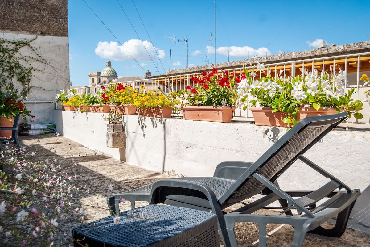 A rooftop terrace with potted plants, a lounge chair, and a view of a building with a dome.