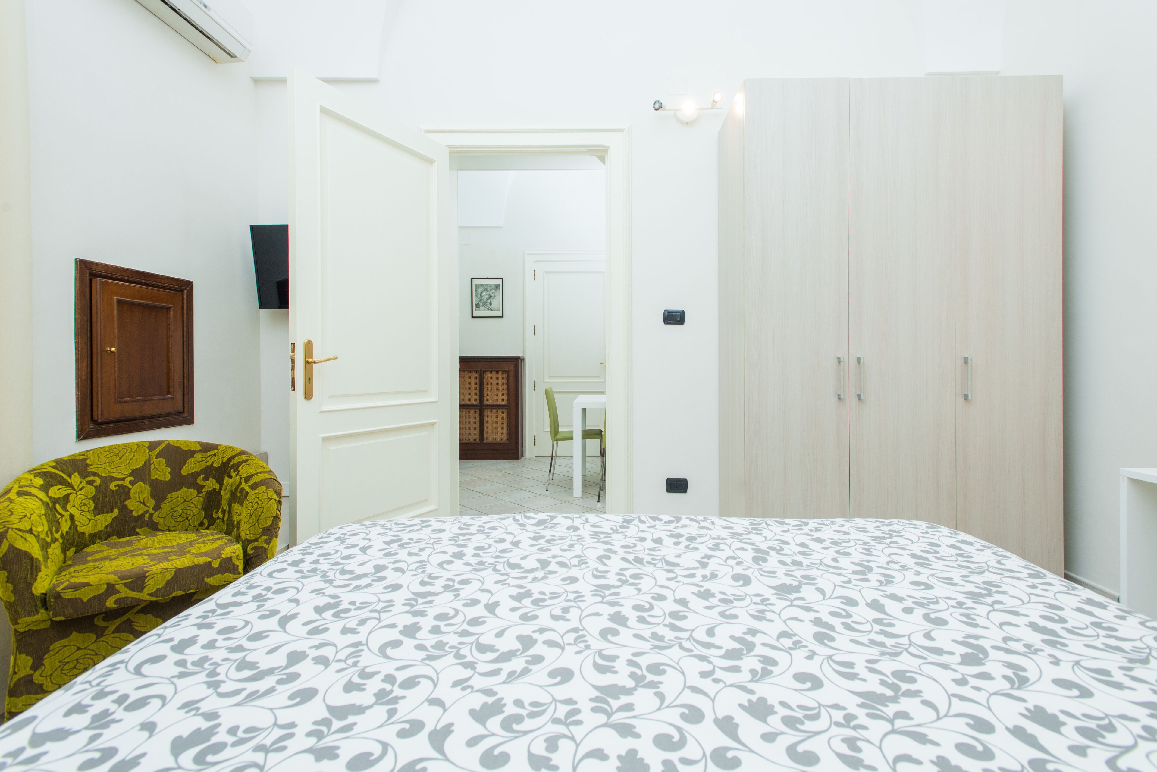 Un dormitorio con cama, armario, silla y puerta que da a otra habitación.