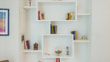 Une pièce avec des étagères blanches où sont rangés des livres, des objets décoratifs et un tableau encadré au mur.