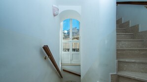 Una escalera con barandilla, una ventana con celosía decorativa y una puerta con pomo de latón.