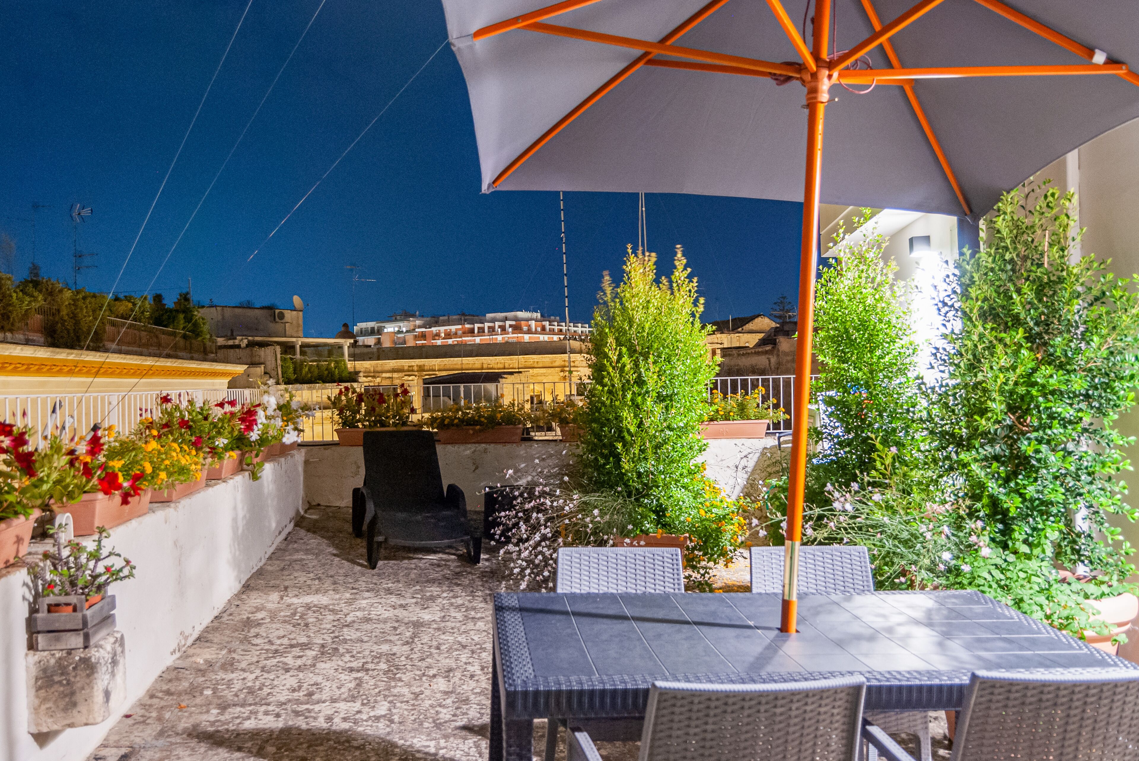 An outdoor patio with a table and chairs, a large umbrella, and potted plants.