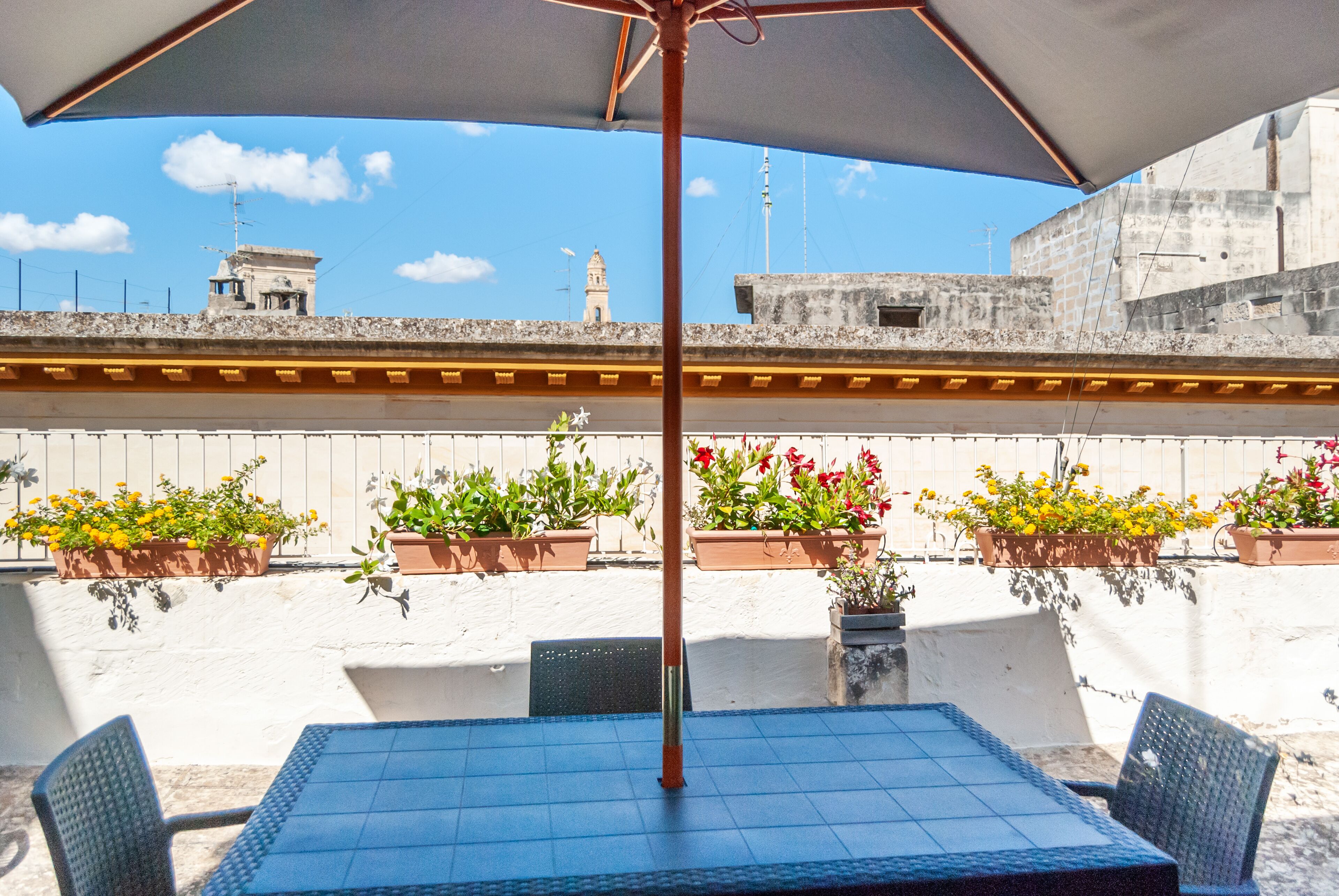 An outdoor patio with a table and chairs, surrounded by potted plants and a large umbrella.