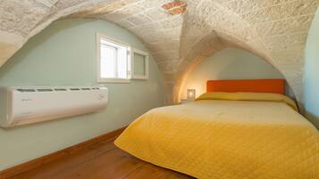 A bedroom with a sloped ceiling, a bed with a yellow quilt, a window, and an air conditioning unit.