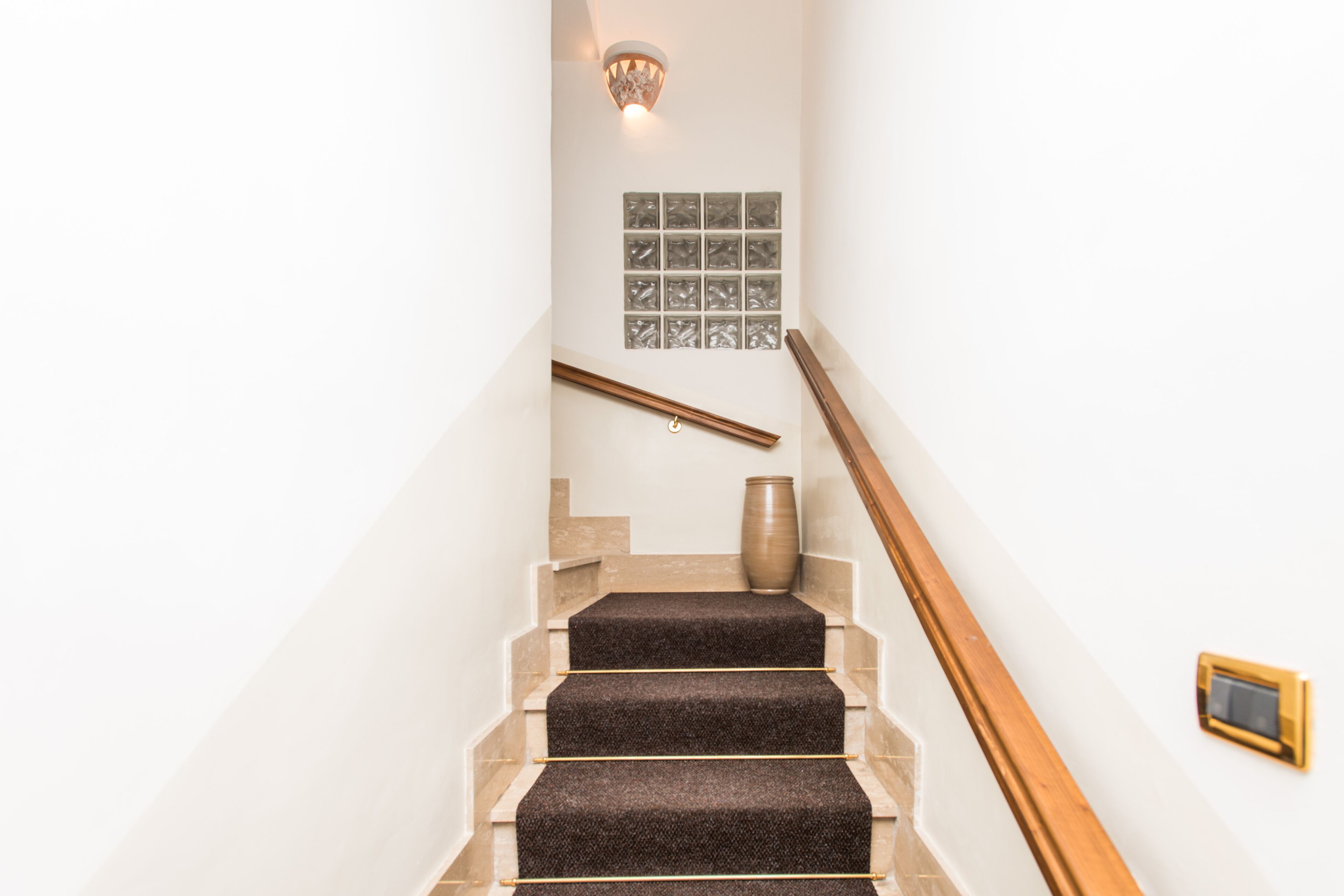 A staircase with a wooden handrail, a vase, and a wall-mounted light fixture.