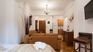 A compact hotel room with a bed, a sofa, a small kitchenette, and a TV mounted on the wall. - New Acropolis Museum Flat (Athens)