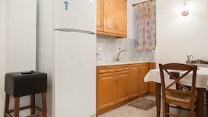 A kitchen with wooden cabinets, a white refrigerator, a small stool, and a dining table with chairs. - New Acropolis Museum Flat (Athens)