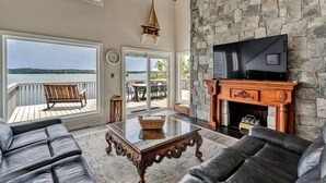 A spacious living room with a stone fireplace, leather sofas, a glass coffee table, and a TV mounted on the wall.